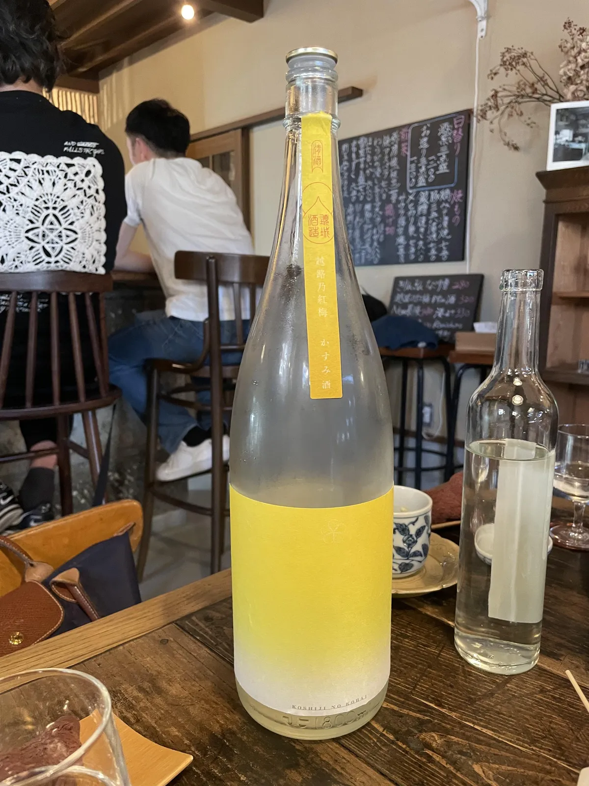 飲食店内のテーブルに置かれた、黄色いラベルが印象的な越路乃紅梅 かすみ酒の一升瓶