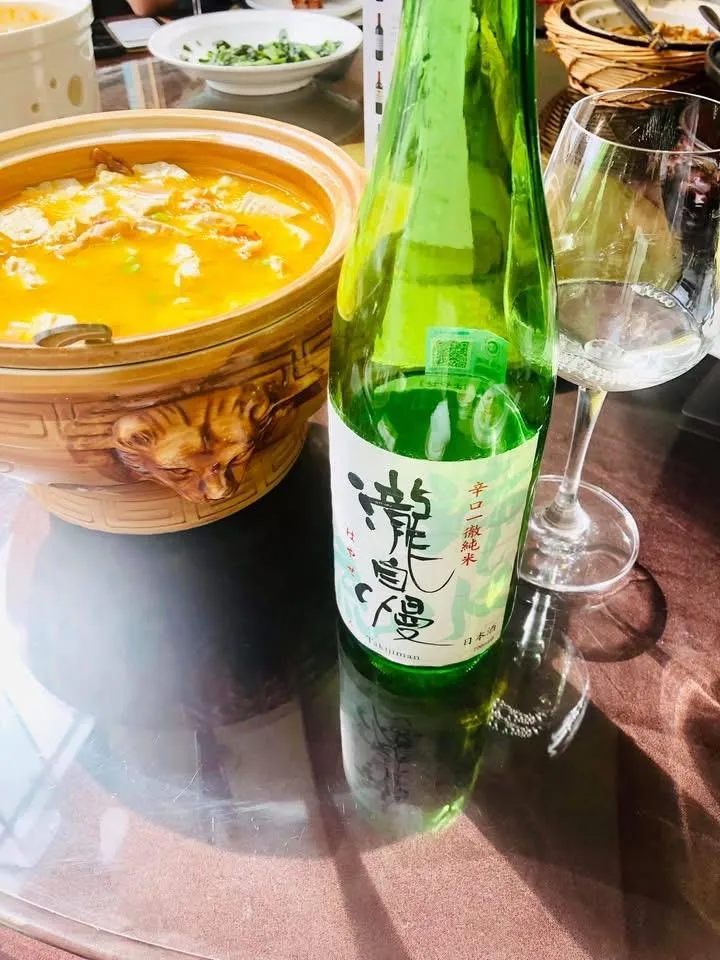 中華料理の鍋の横に置かれた、瀧自慢 滝水流のボトルとワイングラス