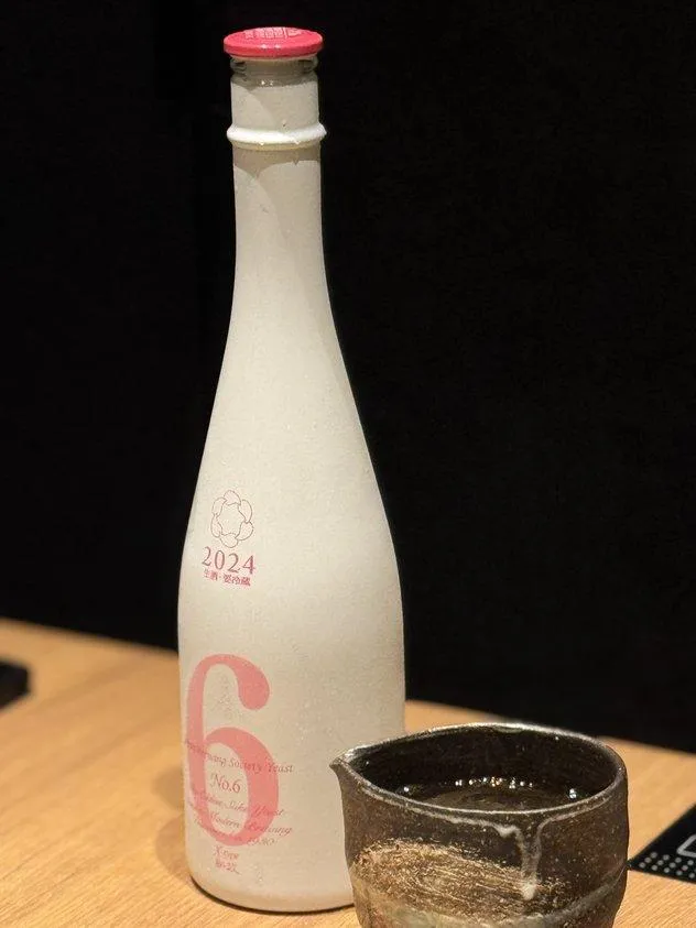 新政酒造のNo.6 X-typeの白いボトルと、お酒が注がれた黒っぽい陶器の器