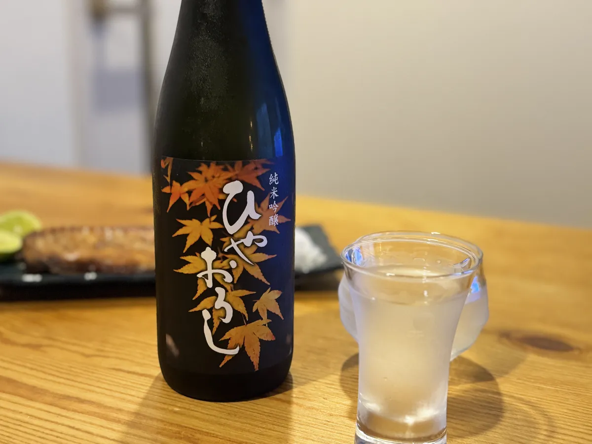 秋らしい紅葉のラベルが印象的なボトルと、グラスに注がれたお酒